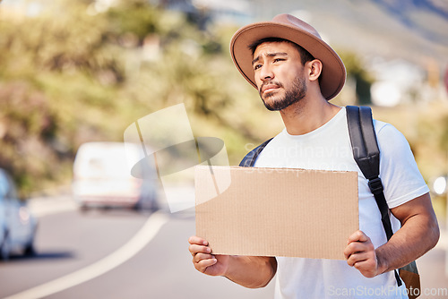 Image of I hope someone stops for me. a young man holding a blank sign while hitchhiking on the side of the road.