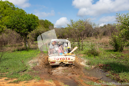 Image of Group of people on the back of a car driving through a muddy forest road. Antsalova, Madagascar