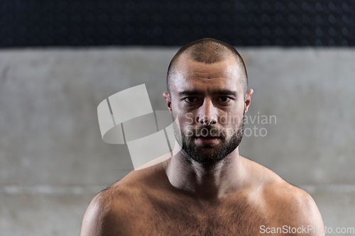 Image of A muscular man poses in the gym, showcasing his strength and dedication to fitness through an impressive physique and glistening sweat on his face.