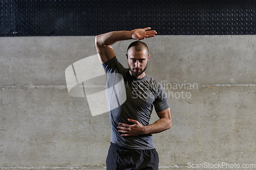 Image of A muscular man working stretching exercises for his arms and body muscles in modern gym