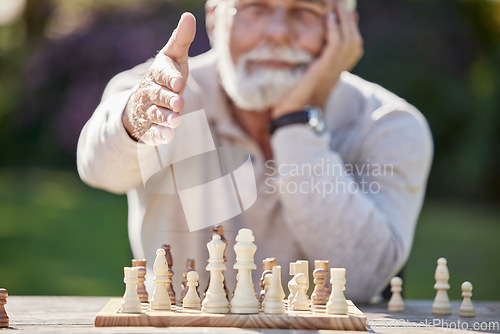 Image of Meet Mr Chess himself. a senior man reaching to shake hands while playing a game of chess outside.