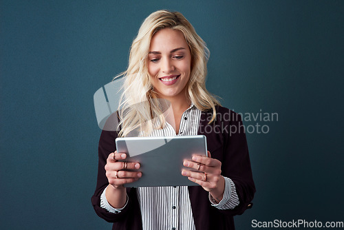 Image of With todays modern age, technology is needed in business. Studio shot of a beautiful young businesswoman using a tablet against a blue background.