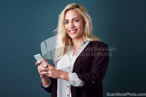 Image of She doesnt wait for opportunity, she creates it. Studio shot of a beautiful young businesswoman using a cellphone against a blue background.