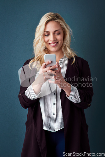 Image of Its all about contacting the correct clients. Studio shot of a beautiful young businesswoman using a cellphone against a blue background.