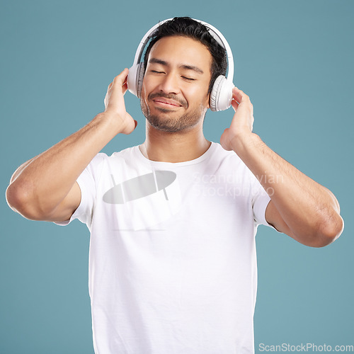 Image of Handsome young mixed race man listening to music while standing in studio isolated against a blue background. Hispanic male streaming his favourite playlist online using wireless headphones