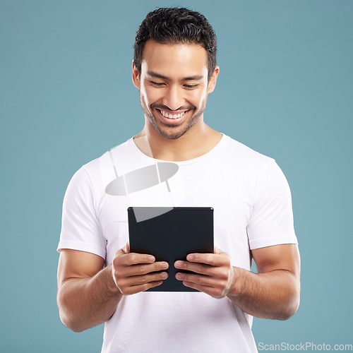 Image of Handsome young mixed race man using his tablet while standing in studio isolated against a blue background. Hispanic male sending an online message, using the internet or browsing social media