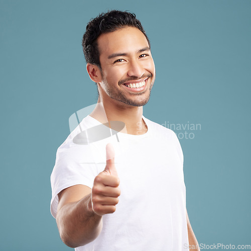 Image of Handsome young mixed race man giving thumbs up while standing in studio isolated against a blue background. Hispanic male showing support or appreciation. Backing or endorsing a product or company