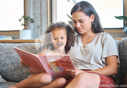 Image of Loving hispanic mother and her little daughter sitting at home and reading a storybook together. Mother teaching little girl to read while sitting on the couch at home