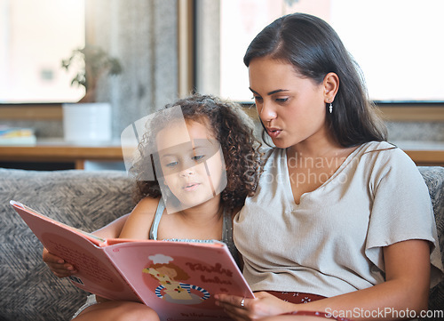 Image of Loving hispanic mother and her little daughter sitting at home and reading a storybook together. Mother teaching little girl to read while sitting on the couch at home