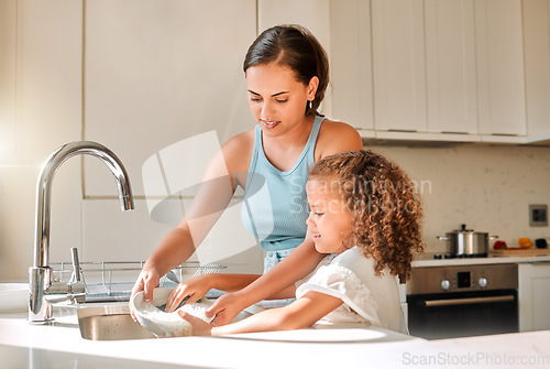 Image of Little girl helping her mother with household chores at home. Happy mom and daughter washing dishes in the kitchen together. Kid learning to be responsible by doing tasks