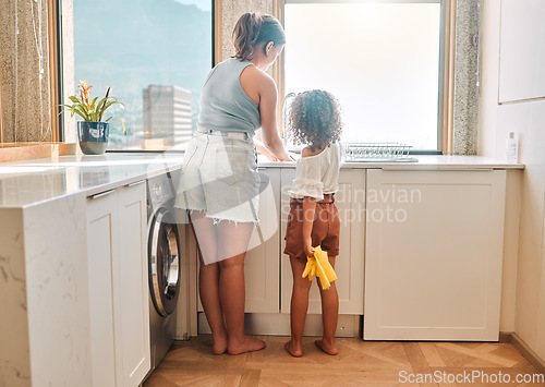 Image of Little girl helping her mother with household chores at home. Happy mom and daughter washing dishes in the kitchen together. Kid learning to be responsible by doing tasks