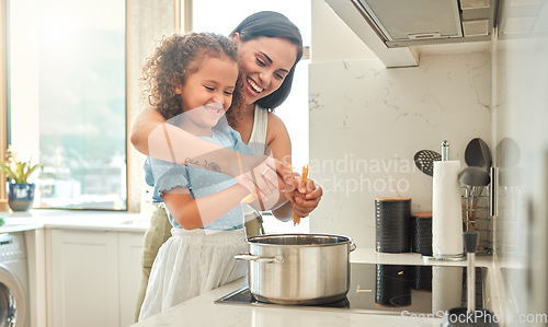 Image of Mother and little daughter cooking together in the kitchen. Mixed race mother and child standing by the stove breaking spaghetti and throwing it in boiling water