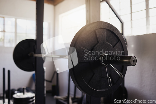 Image of Heavy barbell weights and bar arranged in empty gym with nobody during day. Metal weightlifting equipment organised in a health club and sports centre with no one inside. Healthy exercise routine