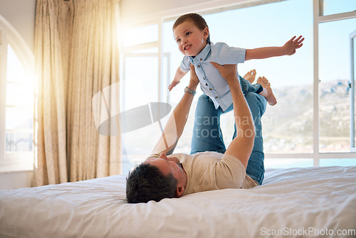 Image of Cheerful caucasian father playfully lifting his son while spending the morning having fun in bed together. Single father playing a game with his little boy at home