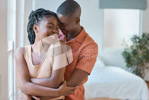 Image of Young affectionate african american couple embracing while relaxing in the bedroom at home. Happy boyfriend hugging girlfriend from behind while sharing an intimate moment in a loving relationship