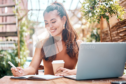 Image of Smiling young businesswoman planning, writing in her diary and drinking coffee while working from a cafe. Freelance hispanic small business owner working on her laptop, making notes.