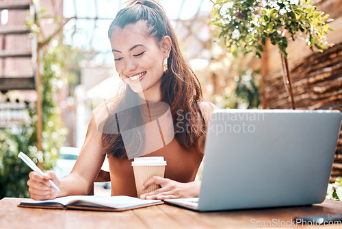 Image of Freelance entrepreneur working in a restaurant, planning, writing notes in her notebook. Smiling young businesswoman drinking coffee, working on her laptop in a cafe. Teleworking businesswoman in caf