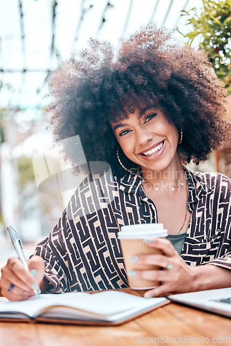 Image of Smiling african american freelancer with curly afro working remotely in a cafe during the day. Mixed race entrepreneur writing notes in a book while enjoying a takeaway coffee. Hispanic businesswoman