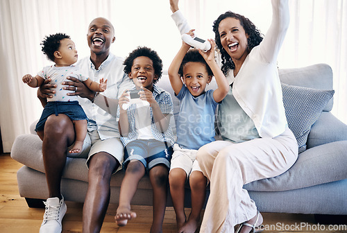 Image of Happy young african american family sitting on a sofa in the living room at home and celebrating a win. Adorable mixed race boys playing video games with consoles while their parents cheer for them