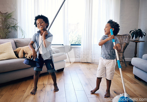 Image of Two mixed race little boys playing with a mop and broom in the lounge at home. Excited siblings having fun playing with cleaning supplies at home. children singing and playing air guitar