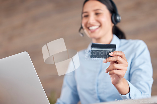 Image of Happy young mixed race call center agent holding a credit card in her hand and working on a laptop while wearing a headset and answering calls in an office at work
