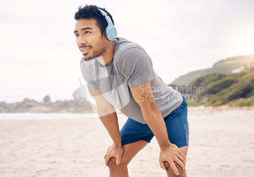 Image of Exercising in nature is a natural antidepressant. a sporty young man wearing headphones and taking a break while exercising on the beach.