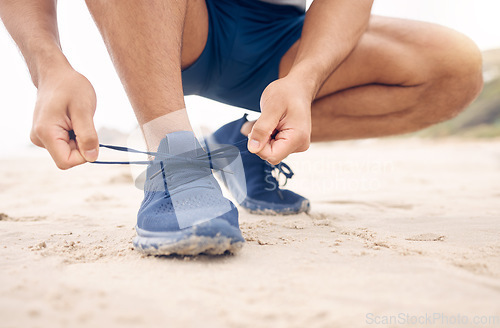 Image of Tie them well to give your feet more support during your runs. Closeup shot of an unrecognisable man tying his laces while exercising on the beach.