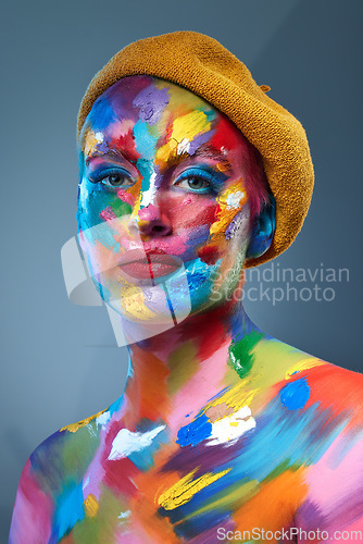 Image of Color and I are one. Studio shot of a young woman posing with multi-coloured paint on her face and a french hat on her head.