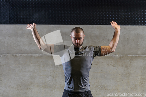 Image of A muscular man working stretching exercises for his arms and body muscles in modern gym