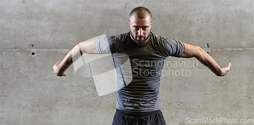 Image of A muscular man working stretching exercises for his arms and body muscles in modern gym