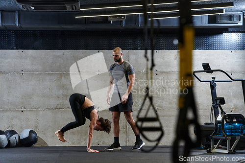 Image of A muscular man assisting a fit woman in a modern gym as they engage in various body exercises and muscle stretches, showcasing their dedication to fitness and benefiting from teamwork and support