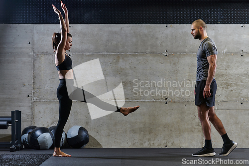 Image of A muscular man assisting a fit woman in a modern gym as they engage in various body exercises and muscle stretches, showcasing their dedication to fitness and benefiting from teamwork and support