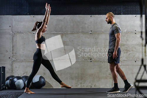 Image of A muscular man assisting a fit woman in a modern gym as they engage in various body exercises and muscle stretches, showcasing their dedication to fitness and benefiting from teamwork and support