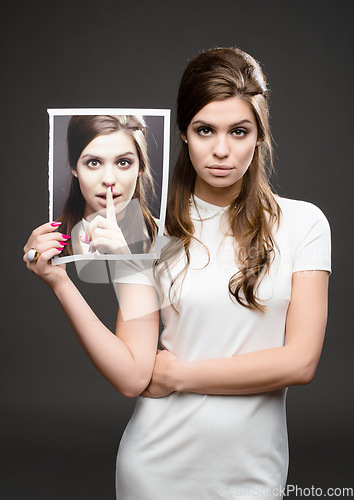 Image of There are two sides to every story. Studio shot of an attractive young woman dressed up in 60’s wear and holding a photograph of herself whispering against a dark background.