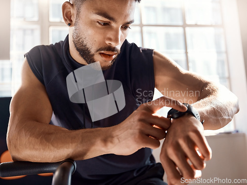 Image of Set the clock for success. a sporty young man checking his watch while exercising in a gym.