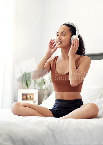 Image of Inhale goodness, exhale negativity. a young woman listening to music while sitting on her bed at home.