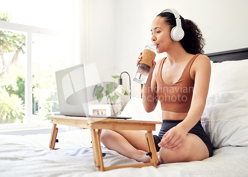 Image of Dont forget to stay hydrated. a young woman using a laptop while sitting on her bed at home.