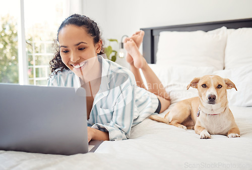 Image of Home is where my dog is. a young woman using a laptop while relaxing on her bed at home.