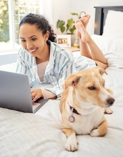 Image of Chilling with my dog. a young woman using a laptop while relaxing on her bed at home.