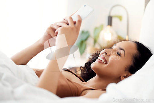 Image of That made me smile. a young woman using a phone while relaxing in bed at home.