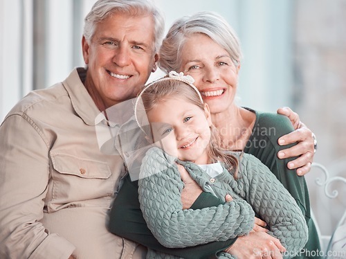 Image of Little girl and her grandparents looking at the camera while sitting together at home. Cute girl bonding with her grandmother and grandfather. Loving couple spending time with their granddaughter