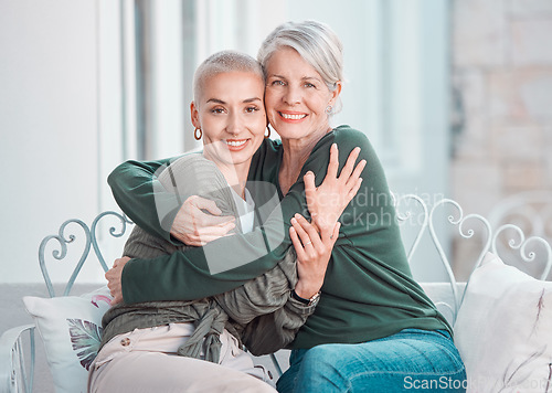 Image of Cheerful senior mother hugging adult daughter. Loving caucasian mom giving her daughter a hug while sitting on a chair together at home. Mature woman looking happy to visit her daughter