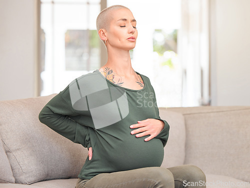 Image of Being pregnant can be tough. an attractive young pregnant woman looking uncomfortable while sitting on the sofa at home.