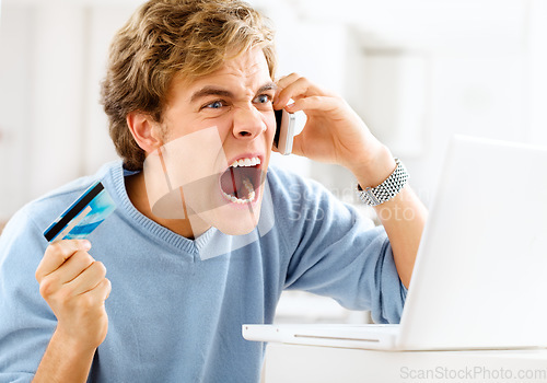 Image of Double deductions ruining his day. a young man making an angry phone call while making online payments.