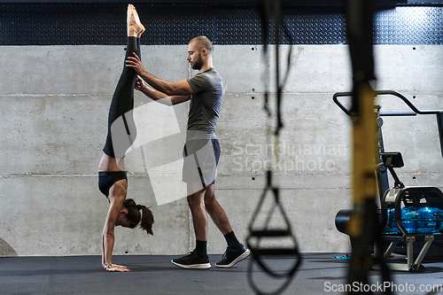 Image of A muscular man assisting a fit woman in a modern gym as they engage in various body exercises and muscle stretches, showcasing their dedication to fitness and benefiting from teamwork and support