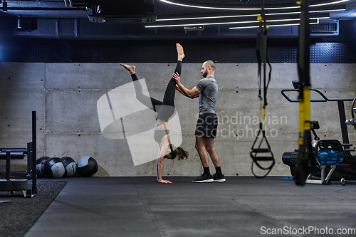 Image of A muscular man assisting a fit woman in a modern gym as they engage in various body exercises and muscle stretches, showcasing their dedication to fitness and benefiting from teamwork and support