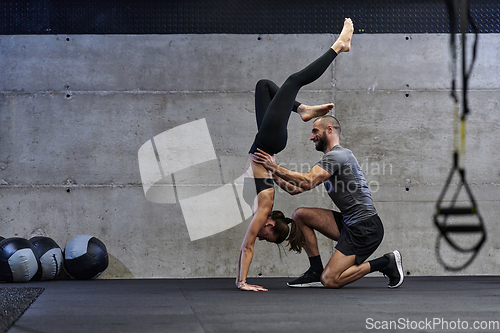 Image of A muscular man assisting a fit woman in a modern gym as they engage in various body exercises and muscle stretches, showcasing their dedication to fitness and benefiting from teamwork and support