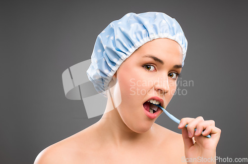 Image of Brushing your teeth can be so arduous. a young woman brushing her teeth against a studio background.