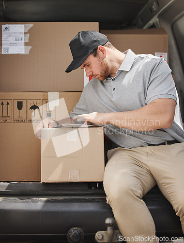 Image of Marking off deliveries as he goes. a handsome young delivery man using a tablet while sitting in the back of his van.