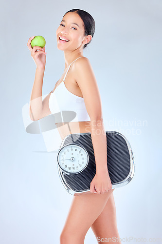 Image of I like my products like my people non-toxic. Studio shot of a young woman tossing an apple while holding a scale against a grey background.